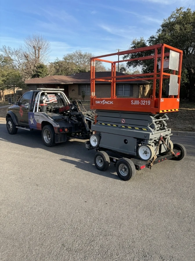 and orange Scissor Lift being towed by black truck of texas patriot towing