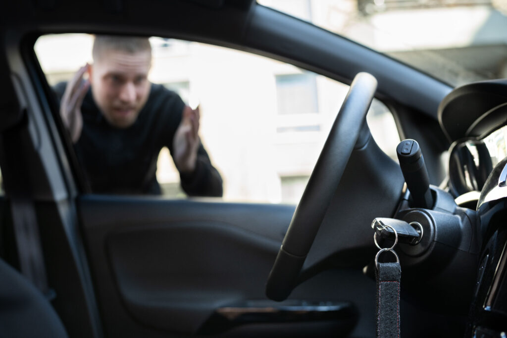 Image of a person locked out of the car standing outside while you can see the car from the inside and the keys hanging in ignition slot